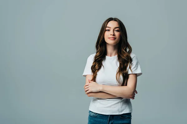 Positive beautiful girl in white t-shirt with crossed arms looking at camera isolated on grey — Stock Photo
