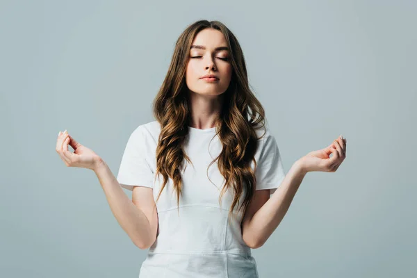 Beautiful girl in white t-shirt meditating with closed eyes isolated on grey — Stock Photo