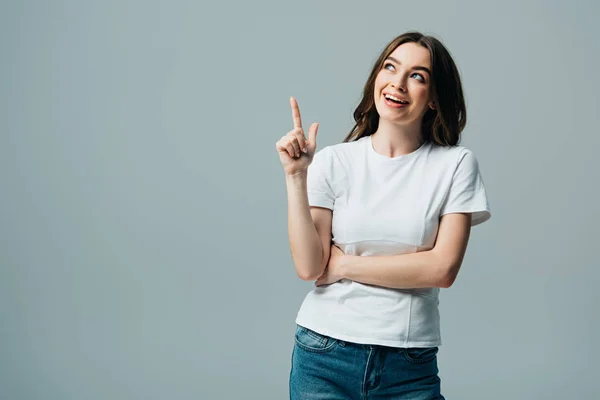 Feliz hermosa chica en camiseta blanca mostrando gesto de idea y mirando hacia otro lado aislado en gris - foto de stock