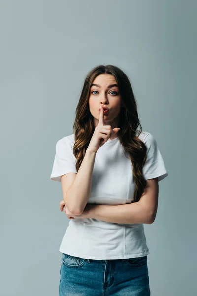 Beautiful girl in white t-shirt showing hush sign isolated on grey — Stock Photo