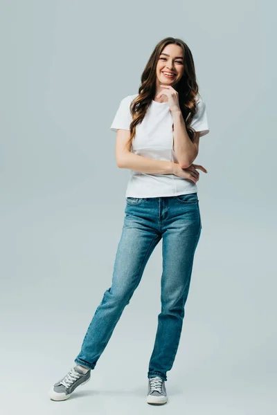 Feliz hermosa chica en camiseta blanca y jeans aislados en gris - foto de stock
