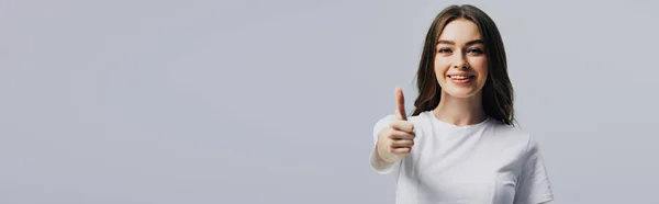 Panoramaaufnahme eines glücklichen schönen Mädchens in weißem T-Shirt, das den Daumen vereinzelt auf grau zeigt — Stockfoto