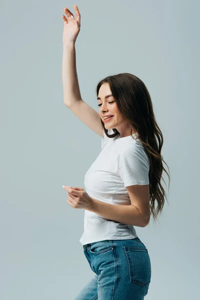 Щаслива красива дівчина в білій футболці танцює ізольовано на сірому — стокове фото