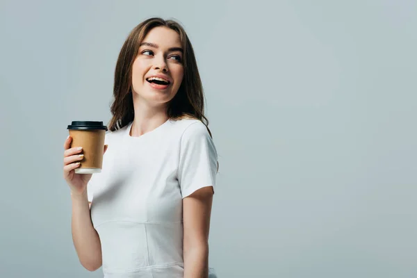 Щаслива красива дівчина в білій футболці з паперовою чашкою дивиться ізольовано на сірому — стокове фото