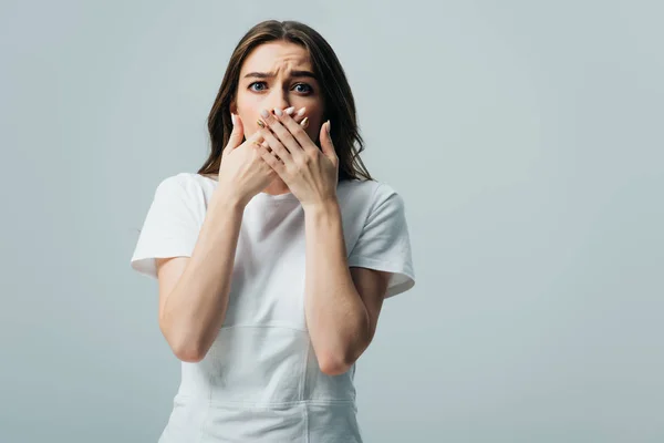 Scared beautiful girl in white t-shirt covering mouth with hands isolated on grey — Stock Photo