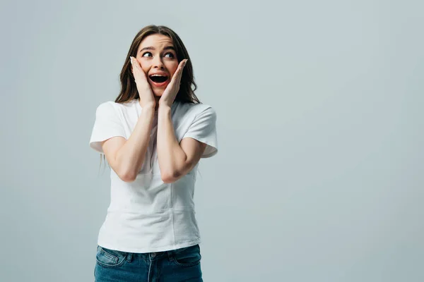 Scioccato felice bella ragazza in bianco t-shirt toccare il viso isolato su grigio — Foto stock