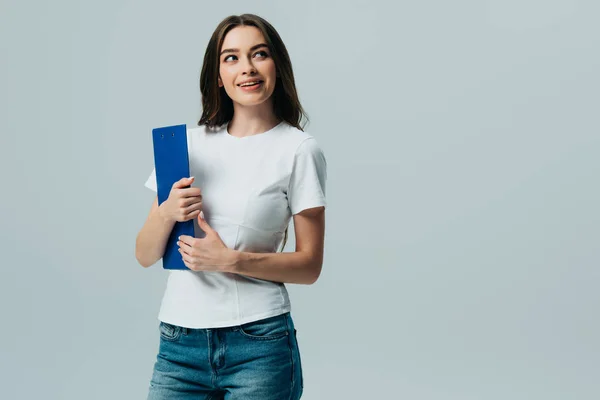 Happy beautiful girl in white t-shirt holding clipboard looking away isolated on grey — Stock Photo