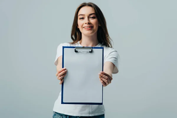 Happy beautiful girl in white t-shirt presenting blank clipboard isolated on grey — Stock Photo