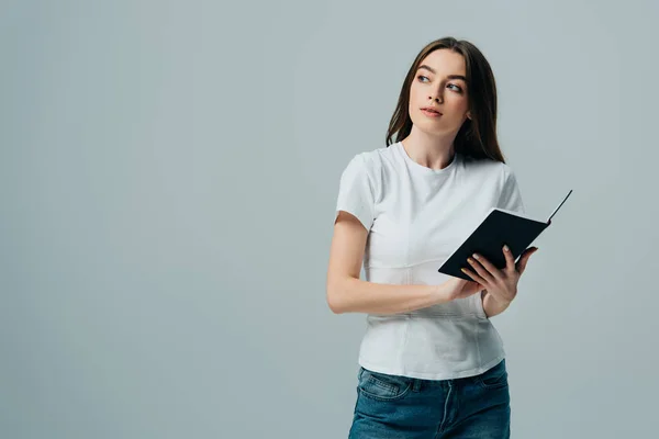 Dreamy beautiful girl in white t-shirt holding notebook isolated on grey — Stock Photo