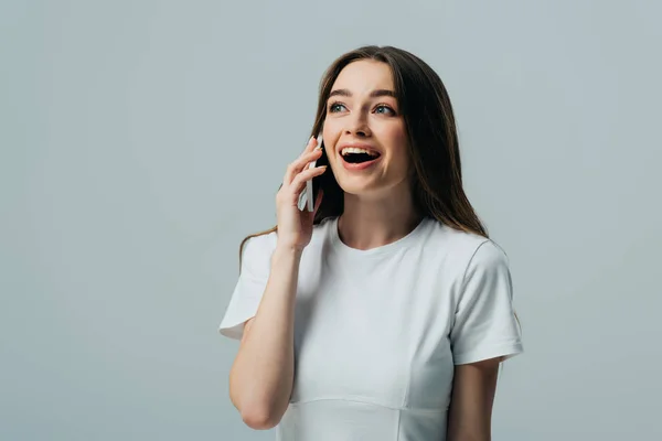 Aufgeregt überrascht schönes Mädchen in weißem T-Shirt spricht auf Smartphone isoliert auf grau — Stockfoto