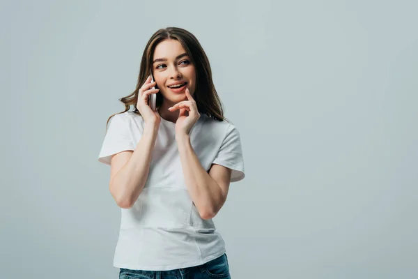 Astuto bella ragazza in bianco t-shirt parlando su smartphone isolato su grigio — Foto stock