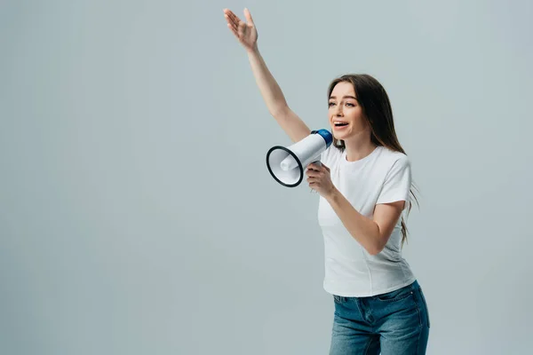 Cheerful young pretty woman speaking in loudspeaker with hand in air isolated on grey — Stock Photo