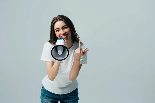 Glückliche junge hübsche Frau mit Lautsprecher zeigt Mittelfinger isoliert auf grau — Stockfoto