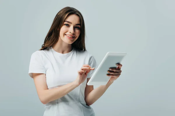 Chica feliz en camiseta blanca sosteniendo tableta digital aislada en gris - foto de stock