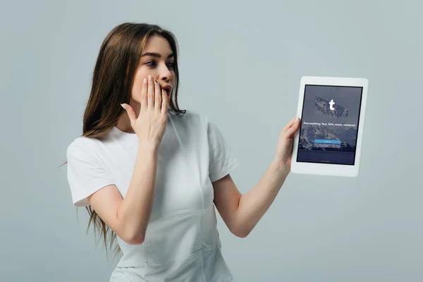 KYIV, UKRAINE - 6 JUIN 2019 : belle fille choquée en t-shirt blanc montrant tablette numérique avec application Tumblr isolée sur gris — Photo de stock