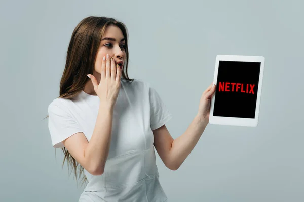 KYIV, UKRAINE - JUNE 6, 2019: shocked beautiful girl in white t-shirt showing digital tablet with Netflix app isolated on grey — Stock Photo