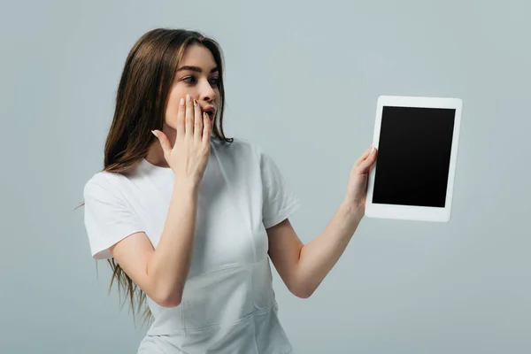 Шокированная девушка в белой футболке показывает цифровой планшет с пустым экраном, изолированным на сером — стоковое фото