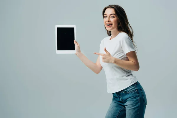 Smiling beautiful girl in white t-shirt pointing with finger at digital tablet with blank screen isolated on grey — Stock Photo