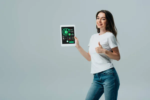 Lächelndes schönes Mädchen in weißem T-Shirt mit Daumen hoch und digitalem Tablet mit Infografik-App isoliert auf grau — Stockfoto