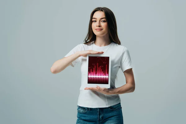 Smiling beautiful girl in white t-shirt showing digital tablet with trading app isolated on grey — Stock Photo