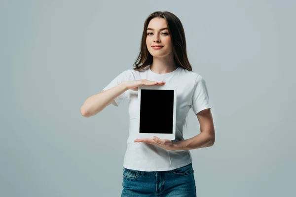 Lächelndes schönes Mädchen in weißem T-Shirt, das ein digitales Tablet mit leerem Bildschirm zeigt, isoliert auf grau — Stockfoto