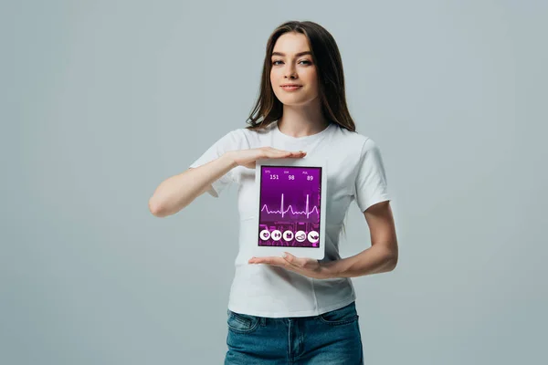 Hermosa chica sonriente en camiseta blanca que muestra tableta digital con aplicación sanitaria aislada en gris - foto de stock