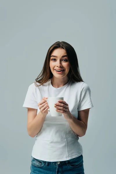 Excited smiling girl in white t-shirt holding white mug isolated on grey — Stock Photo