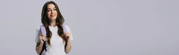 Panoramaaufnahme einer lächelnden hübschen Studentin mit Rucksack isoliert auf grau — Stockfoto