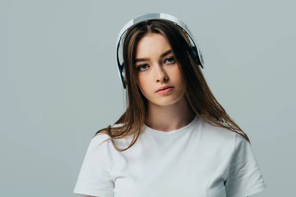 Serious pretty girl listening music in wireless headphones isolated on grey — Stock Photo