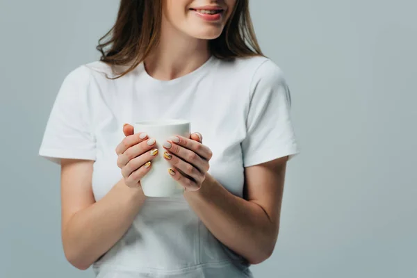 Vista cortada de menina sorridente em t-shirt branca segurando caneca branca isolada em cinza — Fotografia de Stock