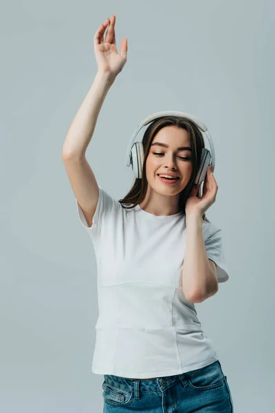 Happy pretty girl listening music in wireless headphones and dancing isolated on grey — Stock Photo