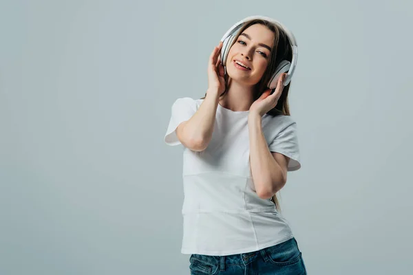 Happy pretty girl listening music in wireless headphones isolated on grey — Stock Photo