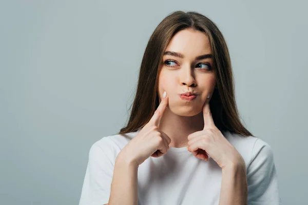 Schöne lustige Mädchen bläst Wangen und sieht weg isoliert auf grau — Stockfoto