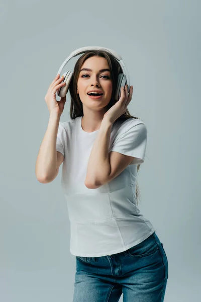 Alegre chica escuchando música en auriculares inalámbricos aislados en gris - foto de stock