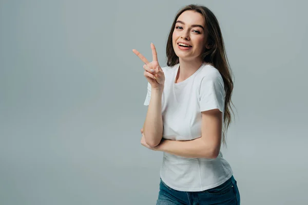 Schöne glückliche Mädchen zeigt Friedenszeichen isoliert auf grau — Stockfoto