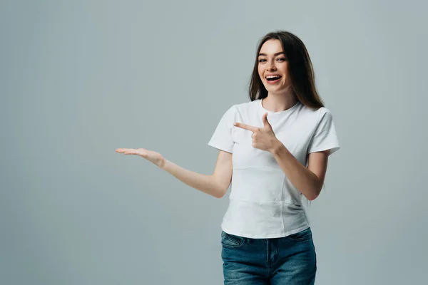 Hermosa chica excitada señalando con la mano y el dedo en el espacio de copia aislado en gris - foto de stock