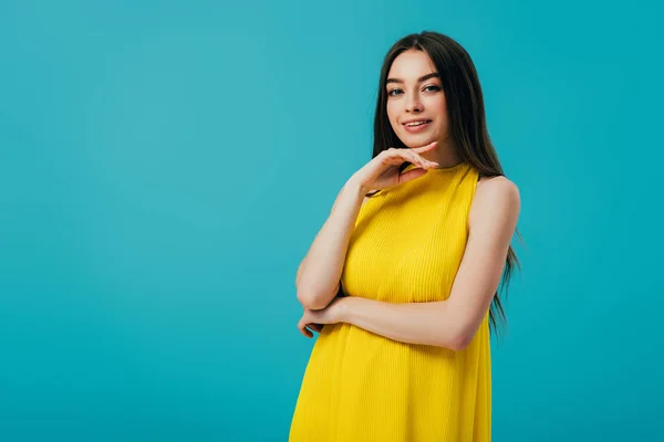 Happy beautiful girl in yellow dress touching face isolated on turquoise — Stock Photo