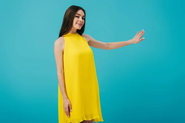 Menina bonita feliz em vestido amarelo gesticulando com a mão isolada em turquesa — Fotografia de Stock