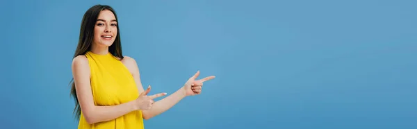 Heureux belle fille en robe jaune pointant avec les doigts de côté isolé sur bleu, panoramique shot — Photo de stock