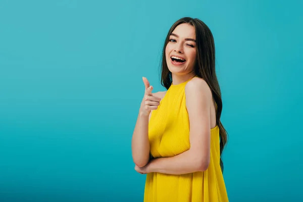 Happy beautiful girl in yellow dress pointing with finger at camera and winking isolated on turquoise — Stock Photo