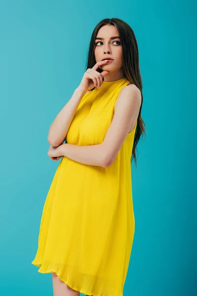 Вдумчивая красивая девушка в желтом платье глядя в сторону изолированы на бирюзовый — стоковое фото