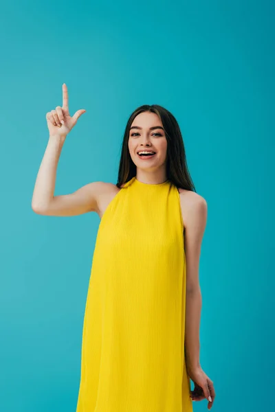 Glücklich schönes Mädchen in gelbem Kleid zeigt mit dem Finger nach oben isoliert auf Türkis — Stockfoto