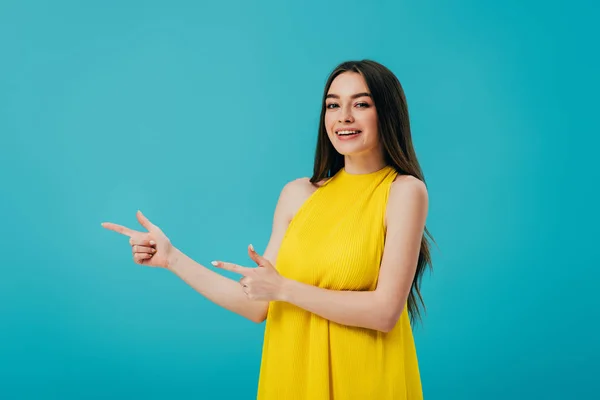 Glücklich schönes Mädchen in gelbem Kleid zeigt mit den Fingern zur Seite isoliert auf Türkis — Stockfoto