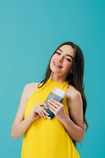 Happy woman in yellow dress holding passport with air ticket isolated on turquoise — Stock Photo