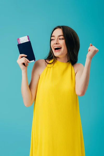 Mulher morena feliz em vestido amarelo segurando passaporte com bilhete de ar e alegria isolada em turquesa — Fotografia de Stock