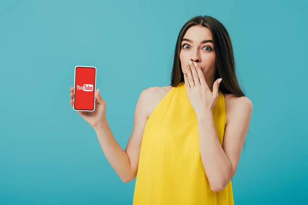 Kyiv, Ukraine - 6. Juni 2019: Schockiertes schönes Mädchen in gelbem Kleid zeigt Smartphone mit Youtube-App isoliert auf Türkis — Stockfoto