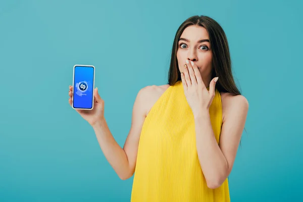 KYIV, UKRAINE - 6 JUIN 2019 : belle fille choquée en robe jaune montrant smartphone avec application shazam isolé sur turquoise — Photo de stock