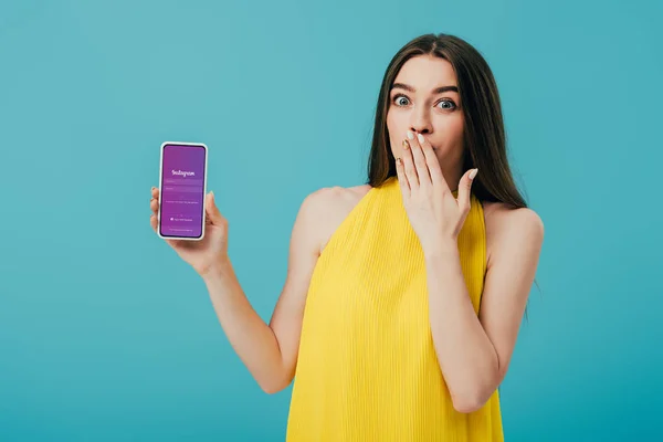 KYIV, UKRAINE - 6 JUIN 2019 : belle fille choquée en robe jaune montrant smartphone avec application Instagram isolé sur turquoise — Photo de stock