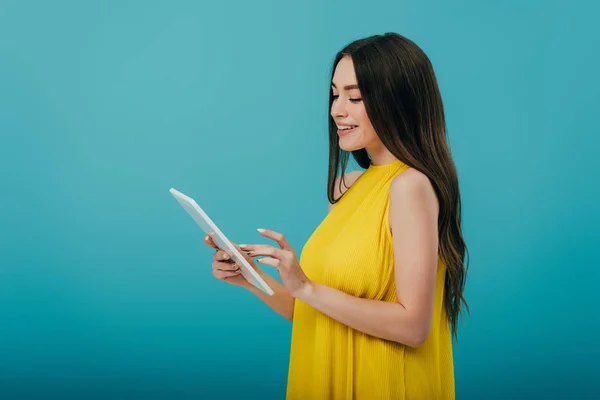 Vue latérale de la jeune fille souriante en robe jaune en utilisant une tablette numérique sur fond turquoise — Photo de stock