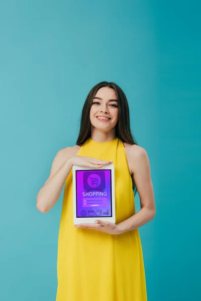 Belle fille brune en robe jaune montrant tablette numérique avec application shopping isolé sur turquoise — Photo de stock